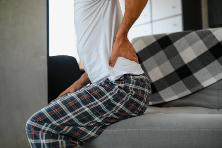 Mann hält seine Hüfte beim Aufstehen vom Sofa aus Schmerz